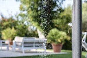 Una fuente con gotas de agua suspendidas, un área de estar exterior blanca y plantas en macetas al fondo.