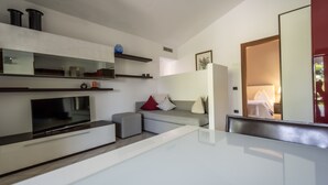 A modern hotel room with a flat-screen TV, built-in shelves, a sofa with cushions, a bedside table, and a large mirror. - Very nice 'villetta' in beautiful and quiet fully garden. (Bardolino)