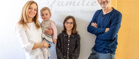 En familj på fyra personer står framför en vägg med texten: ”Här bor familjen Feuerstein/Thurner”.