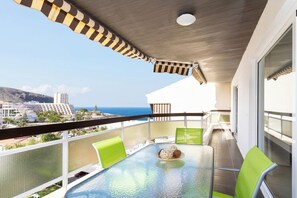 A balcony with a glass table, green chairs, and a view of the ocean and buildings. - Home2Book Beautiful Apart Los Cristianos Pool Wifi (Arona)