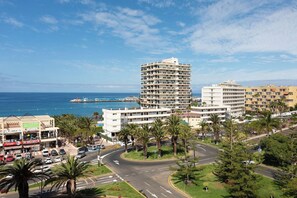 A coastal cityscape with a prominent hotel featuring multiple floors, a roundabout, and palm trees. - Home2Book Beautiful Apart Los Cristianos Pool Wifi (Arona)