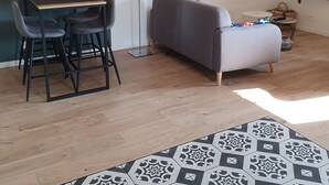 Ein modernes Wohnzimmer mit einer Couch, einem Esstisch mit Stühlen, einem gemusterten Teppich und einem an der Wand befestigten Fernseher.