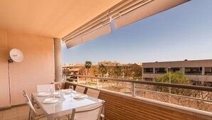 Ein Balkon mit Tisch für zwei Personen, einem weißen Stuhl und Blick auf Gebäude und Bäume.