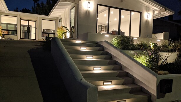 A modern house with a staircase leading to the entrance, illuminated by recessed lighting.