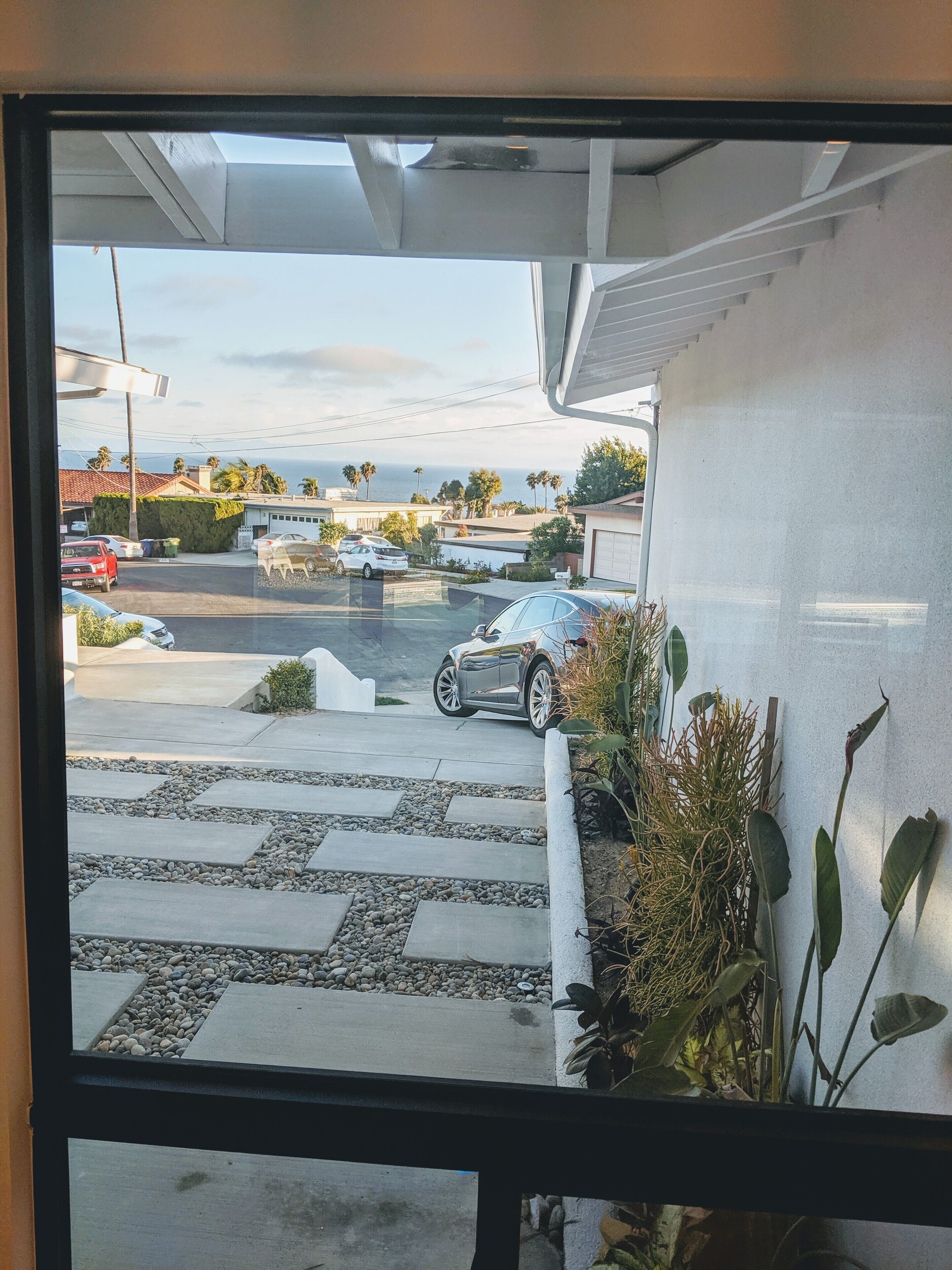 A view from a window of a parking lot with cars, a clear sky, and a distant view of the ocean.