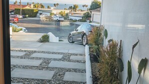 A view from a window of a parking lot with cars, a clear sky, and a distant view of the ocean.