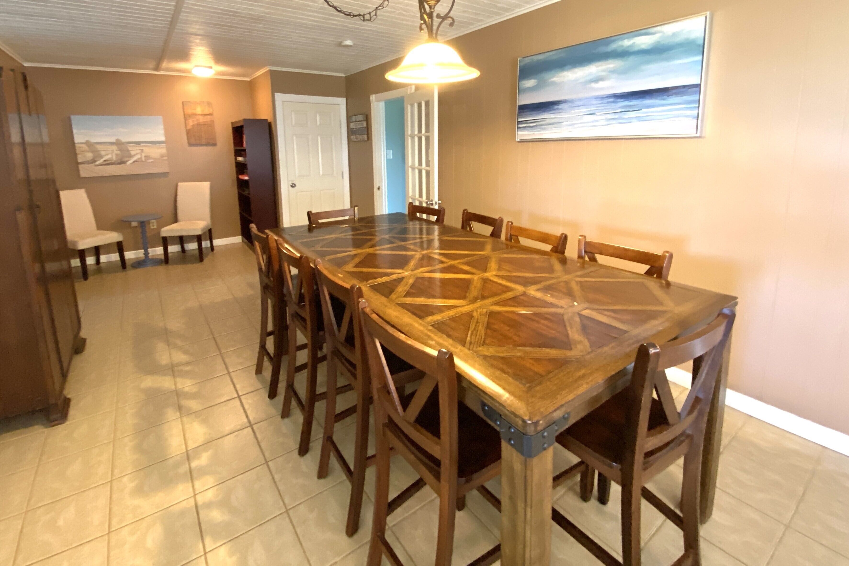Un comedor con una gran mesa de madera rodeada de sillas, una mesita auxiliar y una estantería.