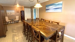 A dining area with a large wooden table surrounded by chairs, a small side table, and a bookshelf.