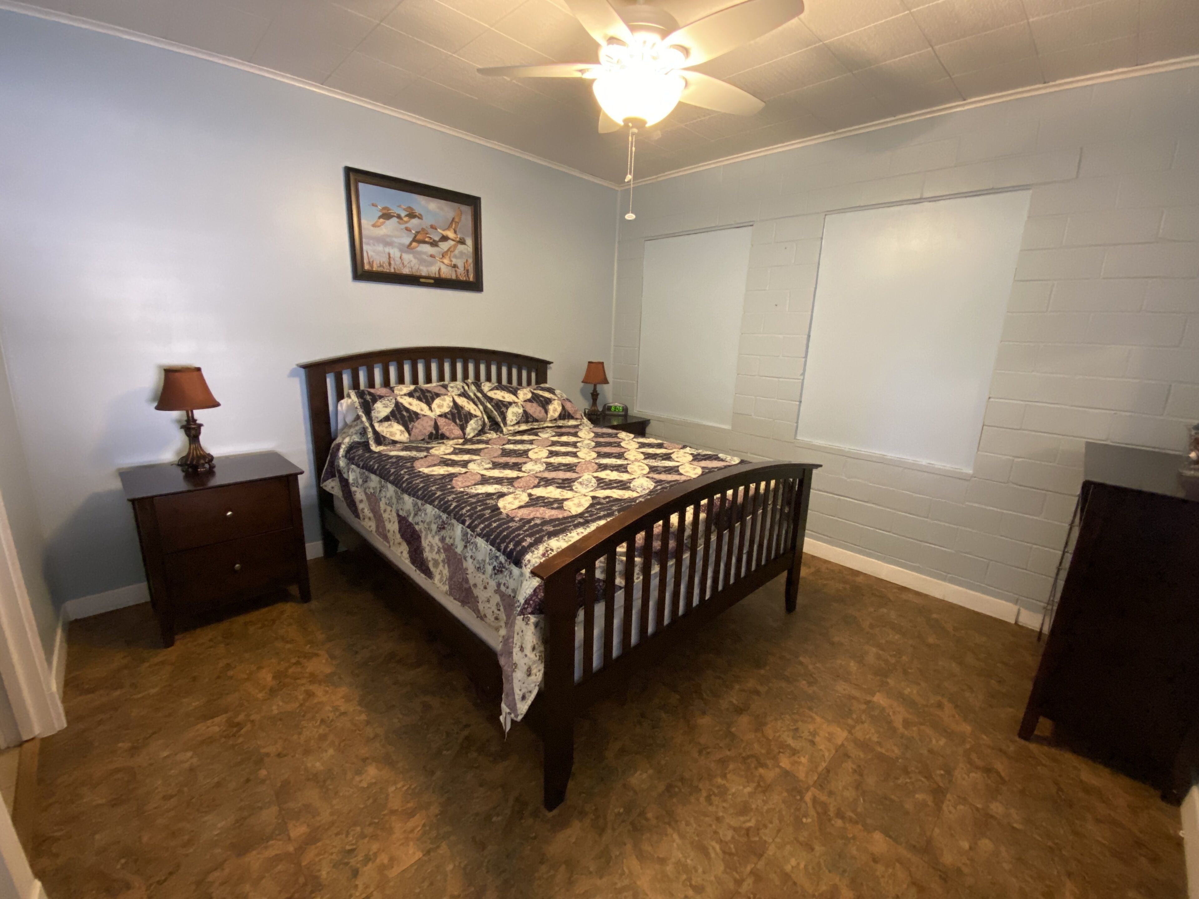 Une chambre à coucher avec un lit, des tables de chevet, un ventilateur de plafond et une fenêtre.