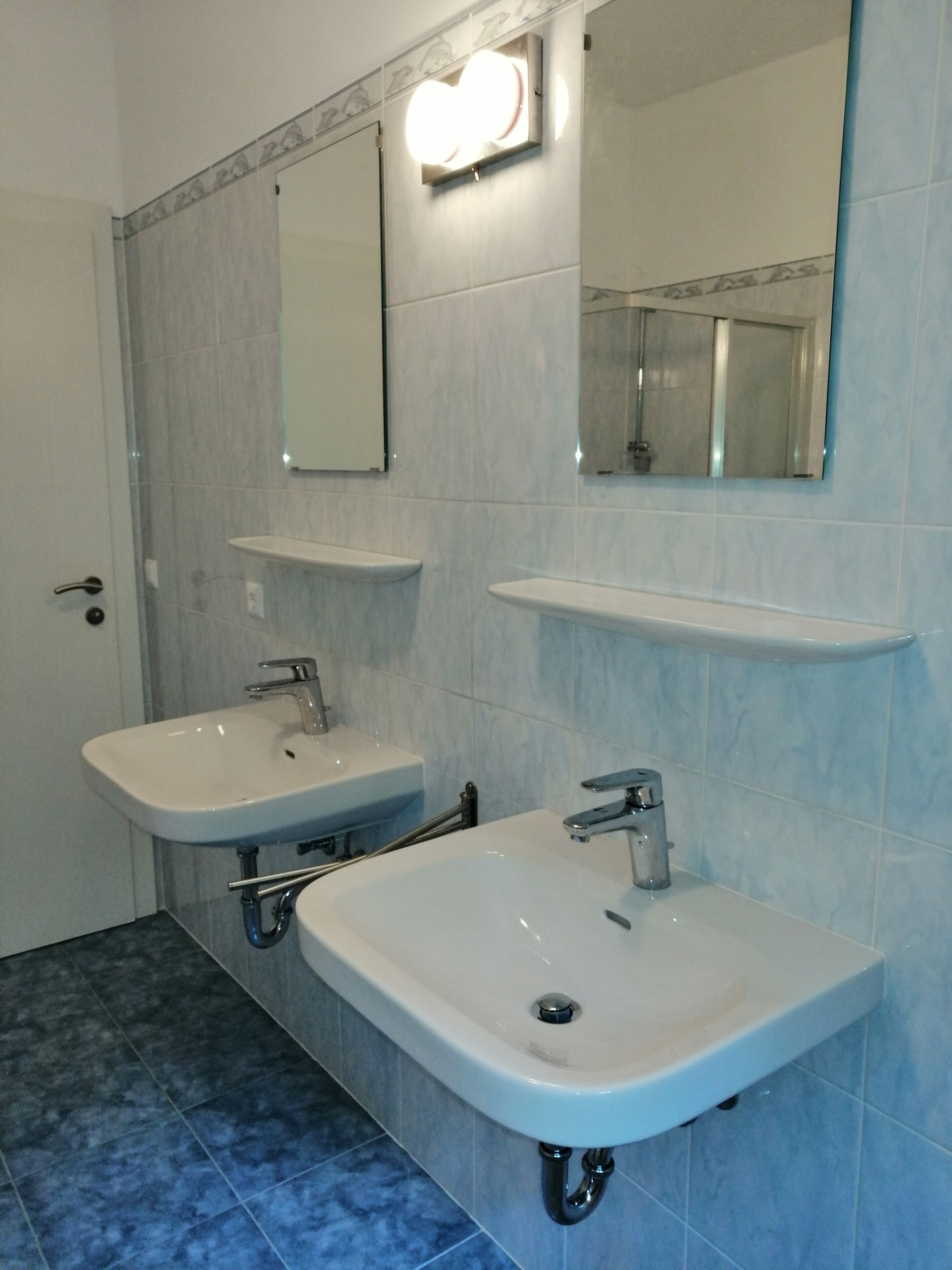 Une salle de bain avec deux lavabos, un miroir et un luminaire placé au-dessus du miroir.