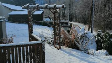 A snow-covered outdoor area with a wooden pergola, a bench, and a pathway leading to a building.