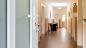 A hallway with a door on the left, a trash bin in the center, and a kitchen area in the background. - 140 m² apartment surrounded by nature (Puchberg am Schneeberg)