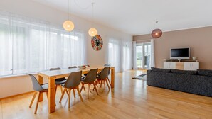 A modern living room with a wooden dining table, chairs, a grey sofa, and a TV on a cabinet. - 140 m² apartment surrounded by nature (Puchberg am Schneeberg)