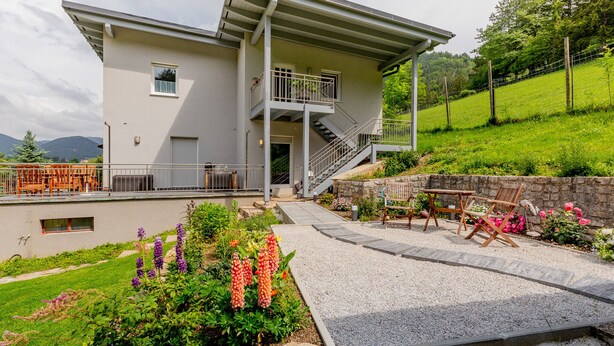 A modern two-story building with a balcony, a staircase, and a garden area with flowers and seating. - 140 m² apartment surrounded by nature (Puchberg am Schneeberg)