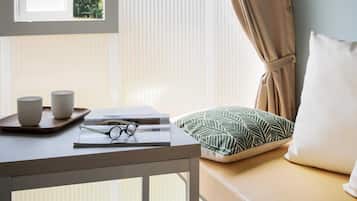 A room with a window, a table with cups and glasses, a pillow, and a bed.