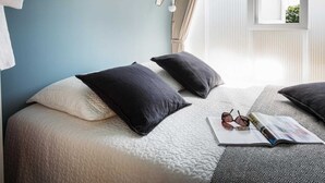 Quarto com duas camas, janela com cortinas e uma revista sobre a cama.