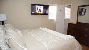 A bedroom with a bed, a television mounted on the wall, a dresser, and a door. - About Legacy House @ Concord (Smyrna)