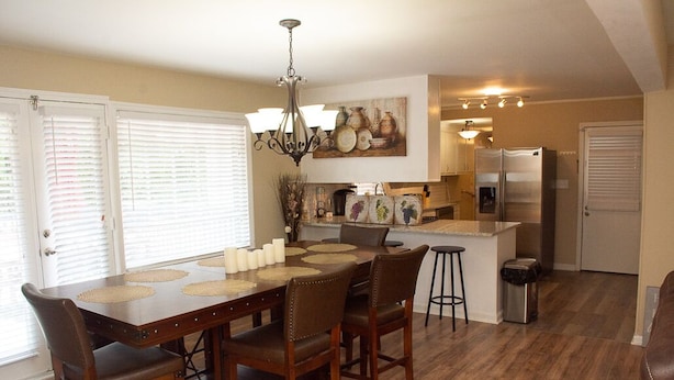 A dining area with a wooden table, chairs, and a chandelier. There is a kitchen area with a refrigerator and a sink. - About Legacy House @ Concord (Smyrna)