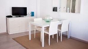 A modern dining area with a white table, four white chairs, a glass bowl, a glass vase, and a flat-screen TV on a white cabinet. - A very special apartment for up to 5 people. (Colònia de Sant Jordi)