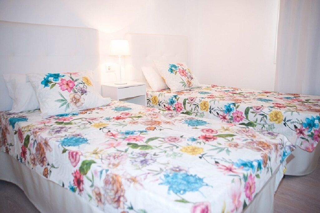 Et hotelværelse med to senge, begge med blomsterprintet sengetøj, et natbord og en lampe.