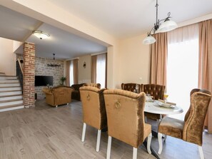 Uma sala de jantar com mesa redonda e cadeiras, lareira de tijolos e escada para outro andar.