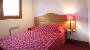 A bedroom with a wooden headboard, a window, a bedside lamp, and a red patterned bedspread. - Spacious apartment for 6 with balcony and parking (Lanslevillard)