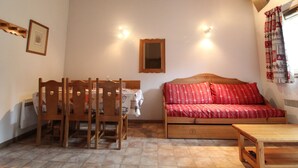 Een gezellige kamer met een houten plafond, een bank met rode kussens met een patroon, een eettafel met stoelen en een spiegel aan de muur.