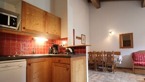 A kitchen with wooden cabinets, a microwave, a coffee maker, and a dining area with a table and chairs. - Spacious apartment for 6 with balcony and parking (Lanslevillard)