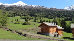A wooden chalet with a balcony, set in a mountainous area with snow-capped peaks in the background. - Spacious apartment for 6 with balcony and parking (Lanslevillard)
