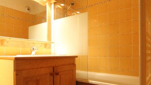 A bathroom with wooden cabinets, a sink, and a bathtub. - Spacious apartment for 6 with balcony and parking (Lanslevillard)