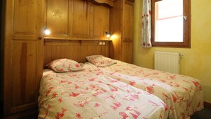 A room with two beds, wooden paneling, a window with curtains, and a radiator.