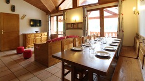 A dining area with a long wooden table set for a meal, wooden cabinets, a television, and a window with curtains.