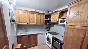 A compact kitchen with wooden cabinets, a dishwasher, a washing machine, and a microwave.