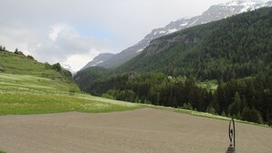 A rural landscape with a dirt field, a small house, and a mountain range in the background.