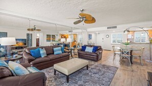 Un vaste espace de vie comprenant un canapé en cuir marron, un pouf beige et une table à manger avec des chaises.