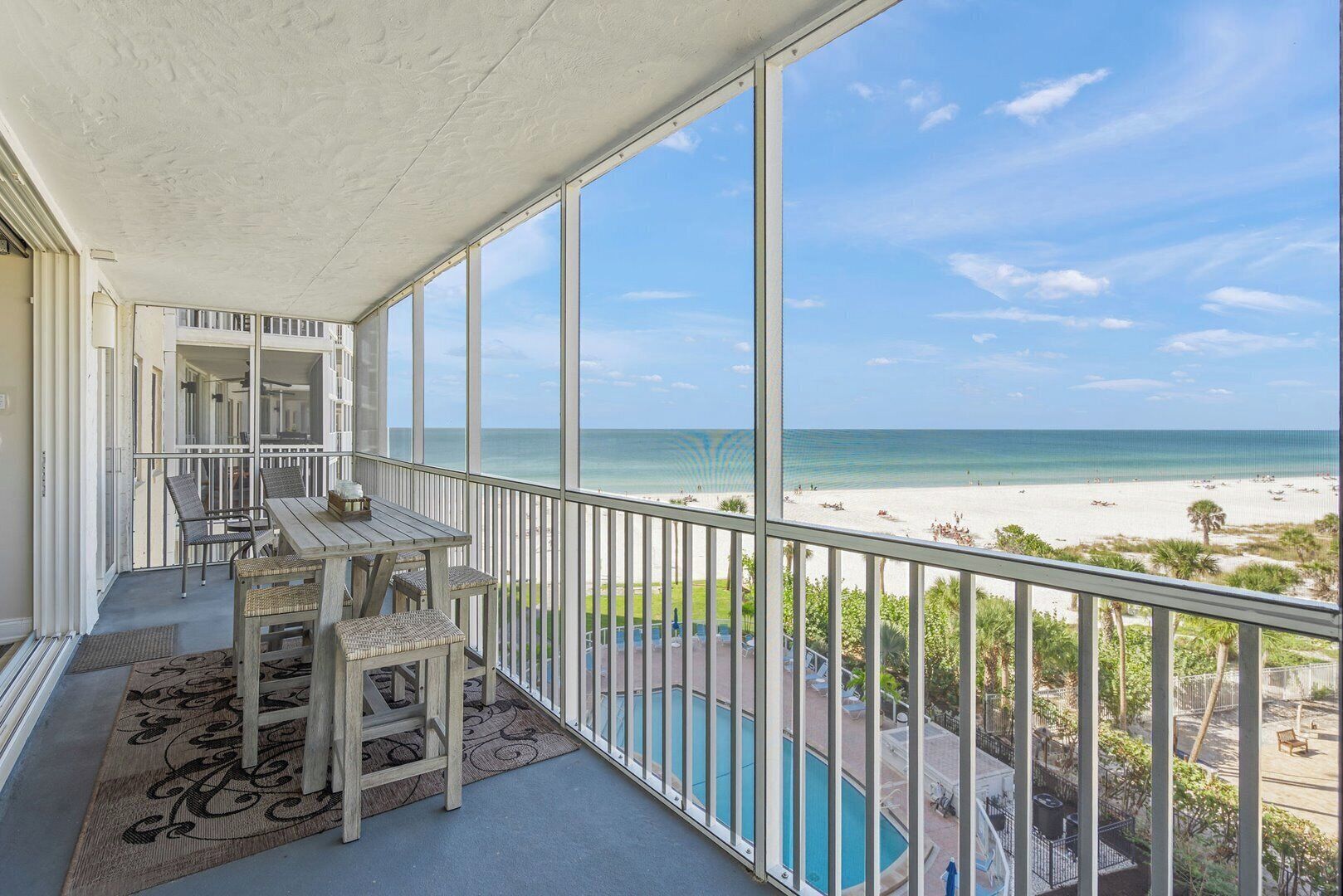 Un balcón con vistas a la playa, una piscina y mobiliario exterior.