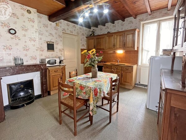 A cozy kitchen with wooden cabinets, a dining table with floral tablecloth, and a vase with flowers.