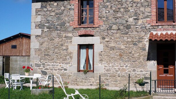 Un edificio de piedra con techo de tejas rojas, puerta de madera y ventana con cortina.