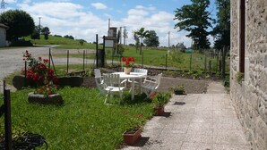 Un patio con mesa y sillas, rodeado de plantas en macetas y un muro de piedra.