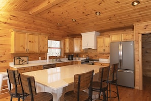 A wooden cabin interior with a kitchen featuring a large island, bar stools, and a refrigerator.