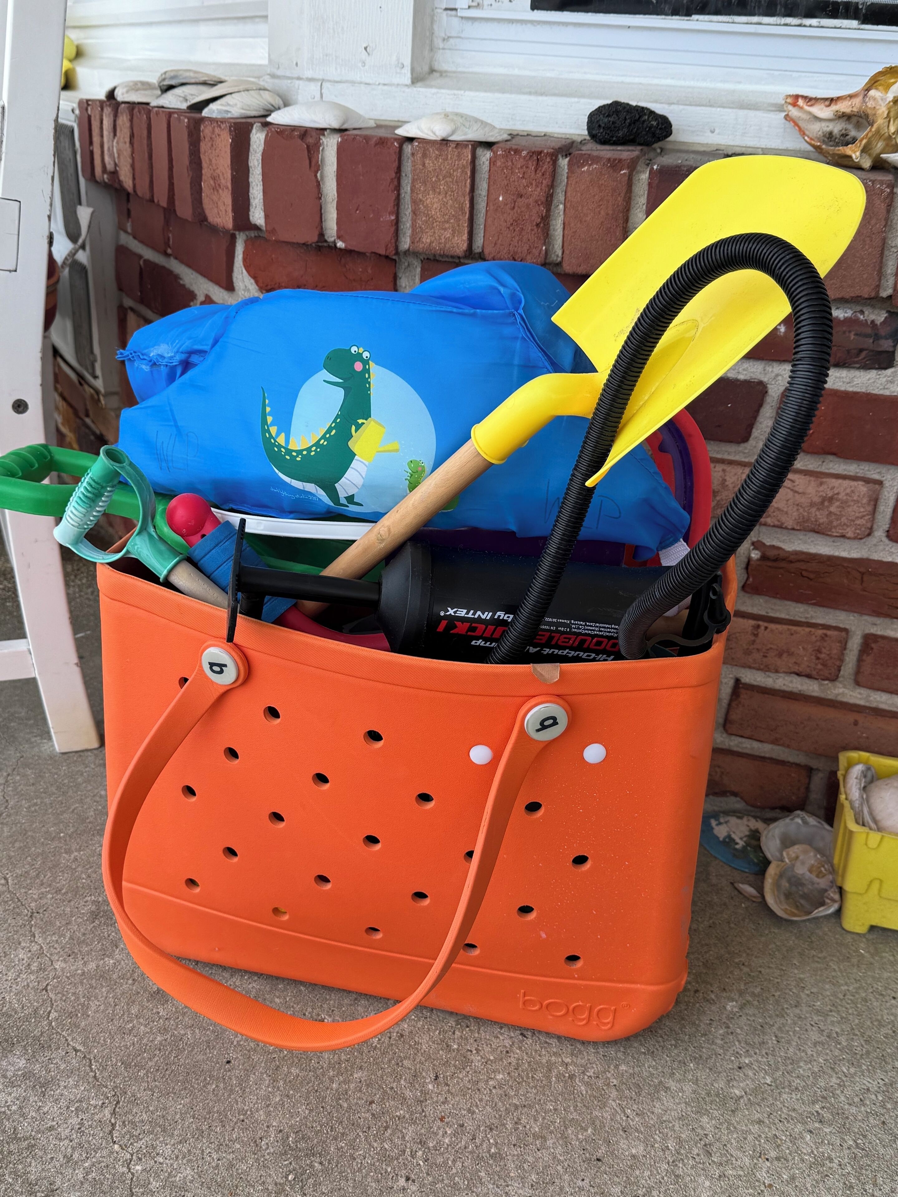 Ein Ordnungsbehälter gefüllt mit verschiedenen Gegenständen, darunter eine blaue Tasche mit einem Dinosaurier-Motiv, ein gelber Schläger und ein grüner Schlauch.