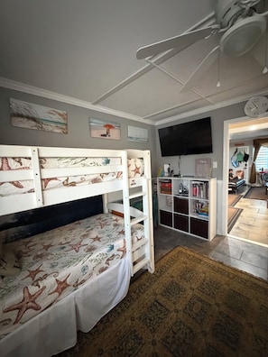 A bunk bed with starfish bedding, a bookshelf, a flat-screen TV, and a ceiling fan in a room with a patterned rug.