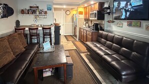 Een woonkamer met een bank, salontafel, televisie en een keuken op de achtergrond.