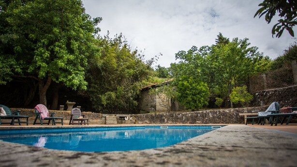 A swimming pool surrounded by stone walls and trees, with lounge chairs and a stone building in the background. - "Casa do moinho" garden, pool and barbecue. (Valença,)