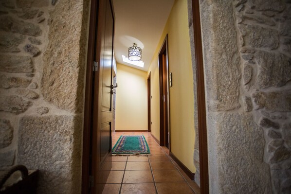 A hallway with stone walls, a tiled floor, and a rug leading to a door. - "Casa do moinho" garden, pool and barbecue. (Valença,)