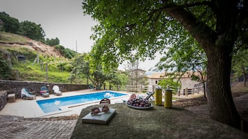 Relax by the serene pool surrounded by a rustic stone wall and shaded by a large tree.