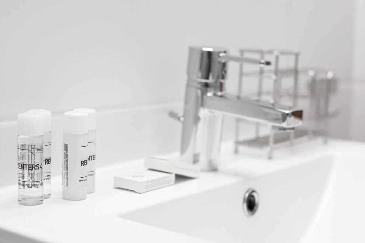 Une salle de bain avec un lavabo blanc, un robinet chromé et trois bouteilles étiquetées « POUR LES LOCATAIRES » sur le comptoir.