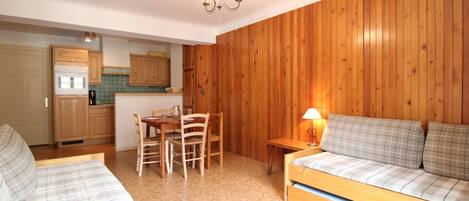 A compact living space with a kitchenette, wooden walls, a dining area, and a sofa.