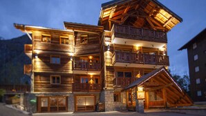 Un edificio de madera de varios pisos con balcones, un cimiento de piedra y una entrada iluminada.
