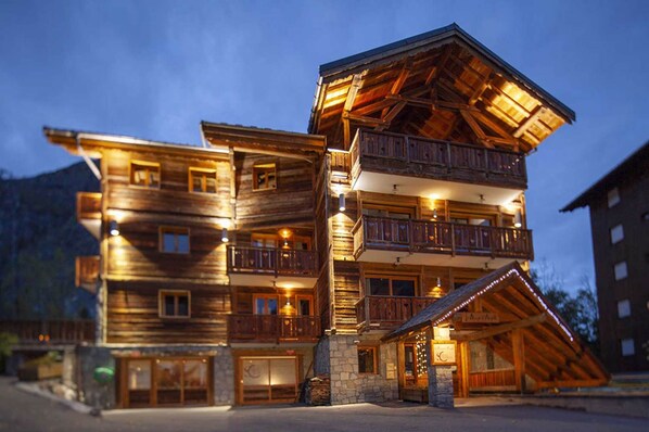 Un edificio de madera de varios pisos con balcones, un cimiento de piedra y una entrada iluminada.